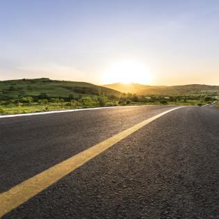 Curved mountain road with sunsetting in the background.