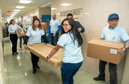 A group of people volunteering at a school, two women are carrying a large cardboard box down a hallway